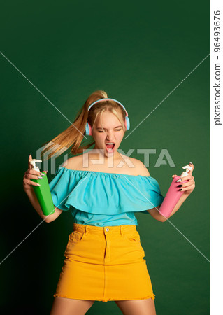 Music, dance. Portrait of young beautiful girl, student in summer outfit posing isolated over green background. Positive emotions, happiness, hobbies and joy Music, dance. Portrait of young beautiful girl, student in summer outfit posing isolated over green background. Positive emotions, happiness, hobbies and joy 96493676