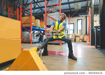 Asian male warehouse worker pulling a pallet truck. Worker working with hand pallet truck unloading cargo boxes on pallet at the warehouse. 96494816