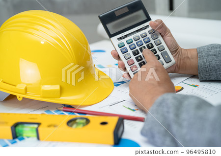 Asian engineer with architectural house plan project blueprint, graph and yellow helmet and engineering construction tools. 96495810