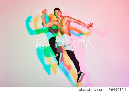 Portrait of young muscular man training, running isolated over pink background in neon light. Multicolored shadow. 96496134