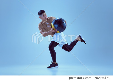 Portrait of young muscular man training, running with med ball isolated over blue background in neon light Portrait of young muscular man training, running with med ball isolated over blue background in neon light 96496160