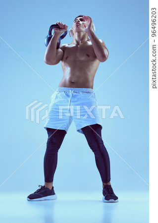 Portrait of young muscular man training, lifting weight isolated over blue background in neon light. Strong hands 96496203