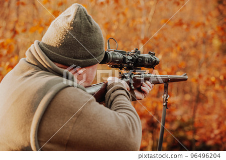 Portrait of hunter or ranger with gun or rifle in the forest looking out or hunting of some venison, hunting period, autumn season, hunting and people concept Portrait of hunter or ranger with gun or rifle in the forest looking out or hunting of some venison, hunting period, autumn season, hunting and people concept 96496204