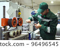 factory worker in a robe and cap checks the performance of the device for the production of cable products from a copper core 96496545