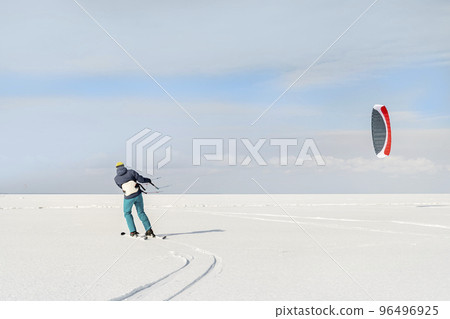 Panoramic view of many people friends enjoy riding kite surf board in warm suit on bright sunny winter day at frozen lake field snowy surface. Wintersport adrenaline fun adventure hobby acitivity Panoramic view of many people friends enjoy riding kite surf board in warm suit on bright sunny winter day at frozen lake field snowy surface. Wintersport adrenaline fun adventure hobby acitivity 96496925