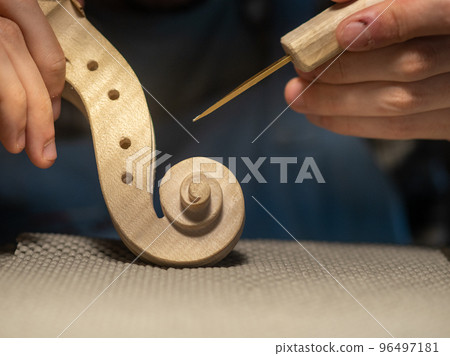 luthier artisan maker sculpting and carving violin scroll and neck with chisel 96497181