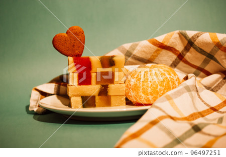 Marzipan turrone on plate, checkered kitchen towel on a green emerald background. Spanish dessert made from almonds, honey, sugar, eggs. Christmas sweets, tangerine, heart-shaped cookie. Cooked indoor 96497251