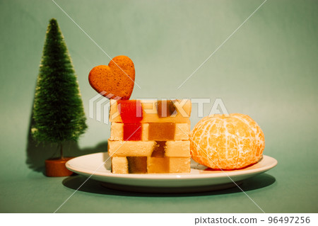 Marzipan marmalade turrone on plate, tangerine on green emerald background. Spanish dessert made from almonds, honey, sugar, eggs. Christmas sweets, heart-shaped cookie. New Year pine tree decor 2023. Marzipan marmalade turrone on plate, tangerine on green emerald background. Spanish dessert made from almonds, honey, sugar, eggs. Christmas sweets, heart-shaped cookie. New Year pine tree decor 2023. 96497256