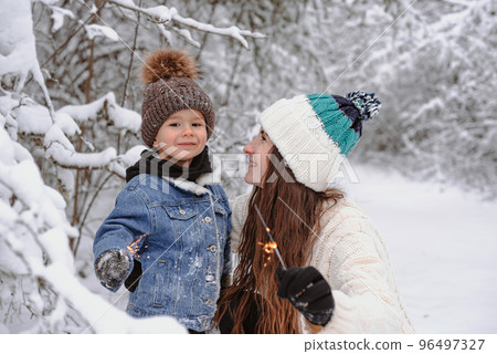 Mom and son are walking in the snow and light sparklers in the forest. Mom and son are walking in the snow and light sparklers in the forest. 96497327