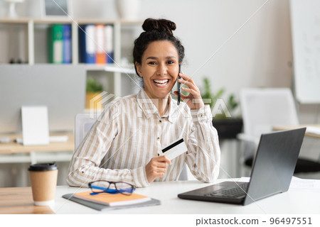 Easy payments concept. Happy businesswoman using credit card and talking on cellphone with customer service 96497551
