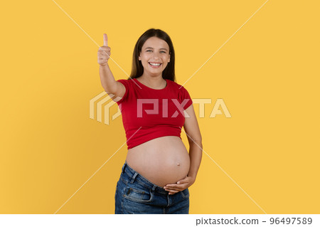 Smiling Young Pregnant Woman Touching Belly And Gesturing Thumb Up At Camera 96497589