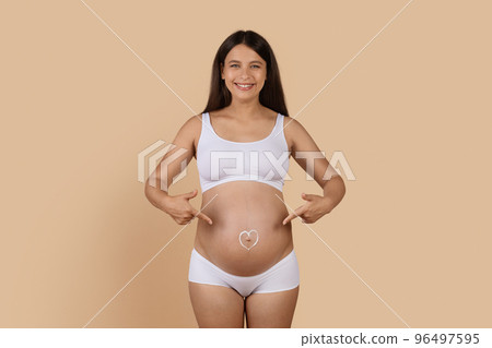 Happy Pregnant Female Pointing At Heart Shape Made Of Cream On Belly 96497595