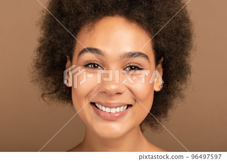 Cheerful millennial african american curly lady with nude makeup looking at camera Cheerful millennial african american curly lady with nude makeup looking at camera 96497597