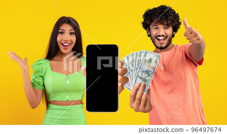 Indian couple betting online, celebrating victory, showing smartphone and cash Indian couple betting online, celebrating victory, showing smartphone and cash 96497674