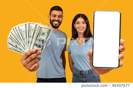 Arab couple betting online, celebrating victory, showing smartphone and cash 96497677