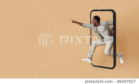 Glad excited millennial black guy with open mouth jumping from huge smartphone screen Glad excited millennial black guy with open mouth jumping from huge smartphone screen 96497827