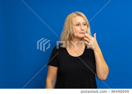 Photo of thoughtful contemplative woman pursing lips with mysterious expression, looking puzzled to side, dressed in t-shirt, isolated over blue background with free copy space. Photo of thoughtful contemplative woman pursing lips with mysterious expression, looking puzzled to side, dressed in t-shirt, isolated over blue background with free copy space. 96498049