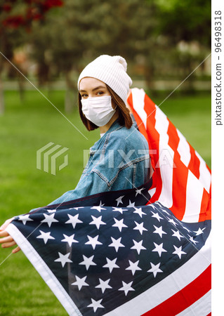 Girl in protective sterile medical mask and with american flag in hand. Quarantine city. Covid -19. Girl in protective sterile medical mask and with american flag in hand. Quarantine city. Covid -19. 96498318