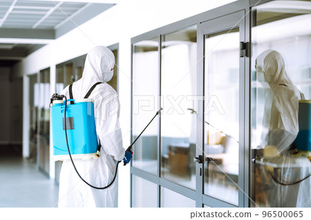 Contractor disinfecting office for COVID-19 coronavirus. A disinfector in a protective suit and mask Contractor disinfecting office for COVID-19 coronavirus. A disinfector in a protective suit and mask 96500065