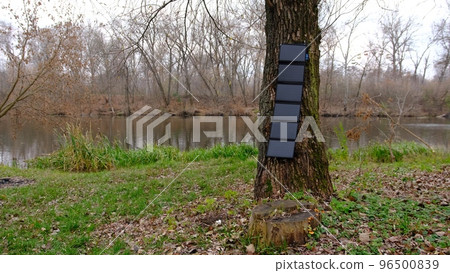 portable solar panel on thr tree charging smartphone by mutlipurpose cable, power bank, watches, laptops nature background. Clean energy for using in camping or at home when NO electricity. 96500839