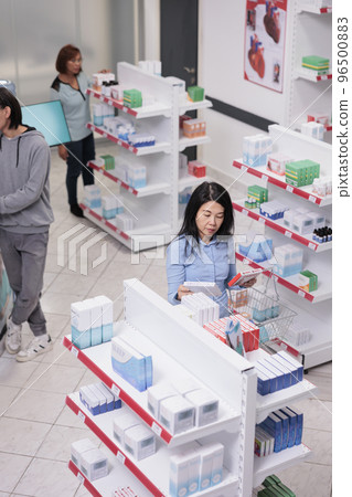 Elderly person reading pills box leaflet before buying healthcare products from drugstore shelves. Pharmacy client looking at medicaments and vitamins packages, cardiology drugs. 96500883