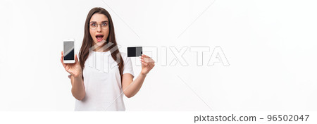 Portrait of excited and happy young woman introduce new application, favorite online store to buy clothes, show mobile phone and credit card, smiling amused, white background 96502047