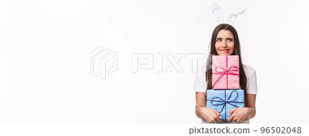 Celebration, holidays and presents concept. Portrait of troubled and doubtful young cute girl in rabbit ears, biting lip and look away, thinking she might forgot buy someone gift, hold presents 96502048