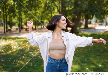 Freedom and people concept. Happy young asian woman dancing in park around trees, smiling and enjoying herself 96502399