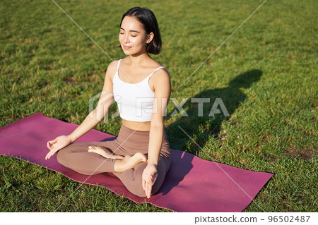 Portrait of smiling asian woman meditating, doing yoga on fresh air, relaxing on rubber mat, exercising in park, breathing air, being calm Portrait of smiling asian woman meditating, doing yoga on fresh air, relaxing on rubber mat, exercising in park, breathing air, being calm 96502487