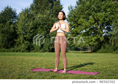 Young asian woman in sportswear, holding hands in namaste gesture, practice yoga, meditating and relaxing on fresh air in park, concept of mindfulness and wellbeing Young asian woman in sportswear, holding hands in namaste gesture, practice yoga, meditating and relaxing on fresh air in park, concept of mindfulness and wellbeing 96502502