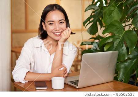 Smiling female manager, freelancer or student sitting with laptop in cafe and working, typing on computer 96502525