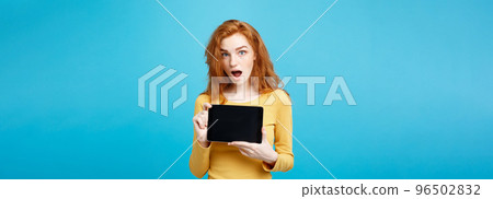 Business Concept - Close up Portrait young beautiful attractive redhair girl smiling showing digital tablet screen on black. Blue Pastel Background. 96502832