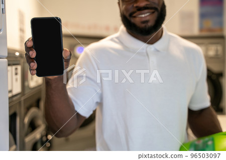 Joyous guy standing in a self-service laundry room 96503097