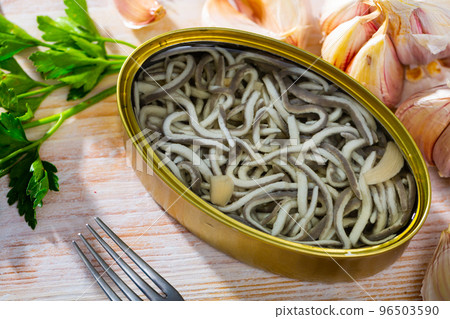 Open tin can of pickled eels and garlic with greens at table Open tin can of pickled eels and garlic with greens at table 96503590