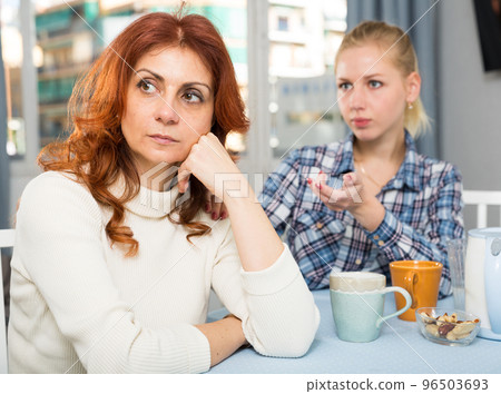Mature female talking with young daughter at table in home Mature female talking with young daughter at table in home 96503693
