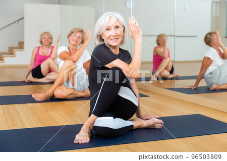 Aged woman doing twisting asana Matsyendrasana in yoga studio 96503809