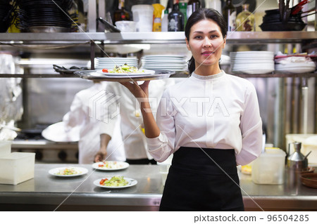 portrait of happy female waitress standing in white kitchen in cafe portrait of happy female waitress standing in white kitchen in cafe 96504285