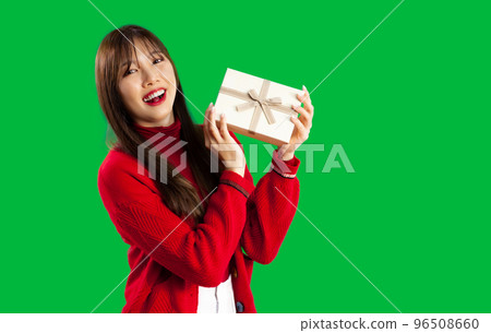 Young pretty asian woman in red sweater posing smiling and holding present box to celebrate Christmas and New Year party on green screen background. Merry Christmas. 96508660