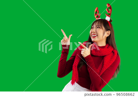 Merry Christmas. asian woman long hair style wearing red long sleeve t shirt and scarf reindeer horns headband posing finger pointing on green screen background. Merry Christmas. asian woman long hair style wearing red long sleeve t shirt and scarf reindeer horns headband posing finger pointing on green screen background. 96508662