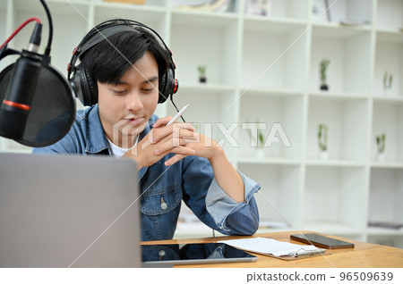 Professional Asian male podcaster or radio host concentrating running his podcast show 96509639
