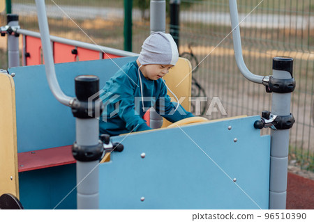 Cute Little boy with down syndrome in a funny hat walks in the playground 96510390