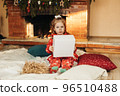 A little girl opens a Christmas present near the Christmas tree. Christmas time, gifts, festive mood. The concept of Christmas and New Year 96510488