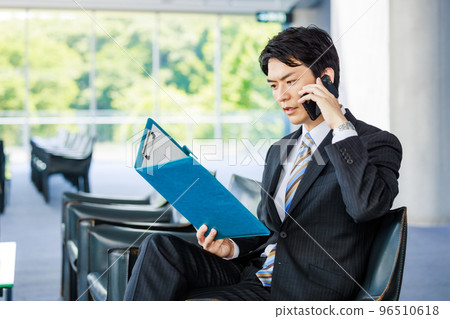 Businessman making a phone call while looking at materials in the lobby 96510618