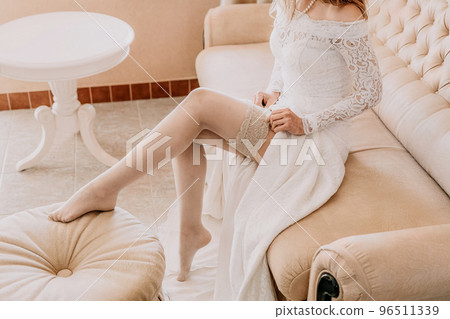 Morning preparation of the bride. Close-up of a bridesmaid, fastening a lot of buttons on the bride's wedding dress. The bride in a white wedding dress with lace standing in the room. Selective focus Morning preparation of the bride. Close-up of a bridesmaid, fastening a lot of buttons on the bride's wedding dress. The bride in a white wedding dress with lace standing in the room. Selective focus 96511339