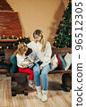 Cute mom and daughter are looking through a family photo album on Christmas Eve, spending time together by the fireplace and the Christmas tree. Christmas, New Year, memories, family evening 96512305