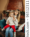 Happy mom and baby daughter reading having fun by the fireplace on Christmas or New Year's Eve. Parenthood, childhood, time together, holidays 96512311