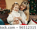 Mom and daughter in casual clothes play and hug against the background of a Christmas tree. Christmas and New Year, Christmas holidays, Christmas time. Childhood, motherhood, time together 96512315
