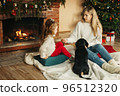 Happy mom and daughter play with their dachshund dog on the floor by the fireplace and Christmas tree 96512320