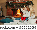 Family mother and child daughter hug and warm up on a winter evening by the fireplace, drink hot cocoa. Christmas Eve or New Year's Eve, Christmas holidays, Christmas time, family evening 96512336