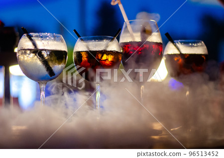 Beautiful row line of different colored alcohol cocktails on a party, martini, vodka,and others on decorated catering bouquet table on open air event, picture with beautiful bokeh 96513452